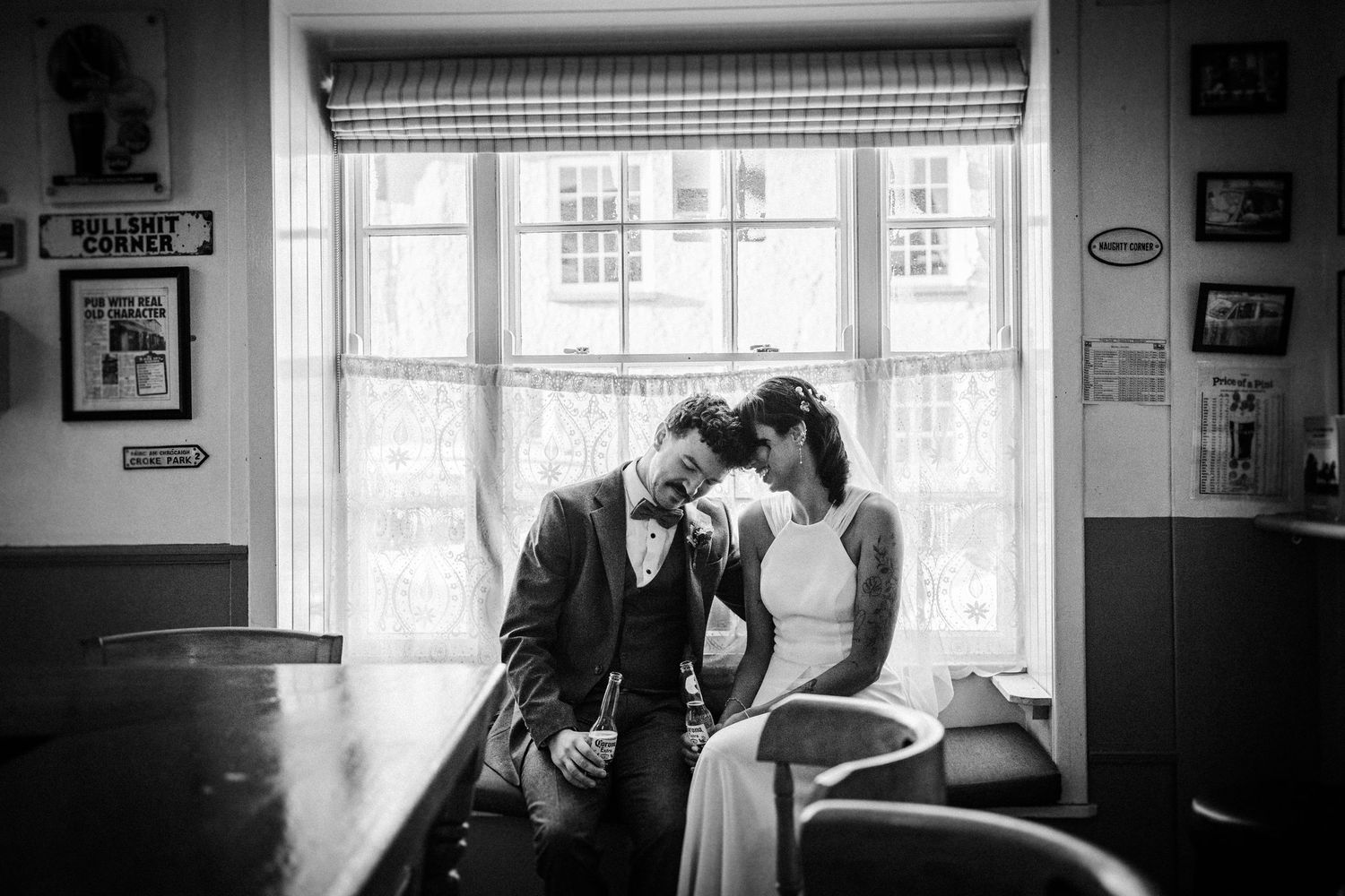 A romantic black and white moment between a couple sitting by a window with lace curtains in vintage decor.