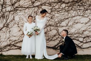 Flower girl, bride and groom fluffing train on gown vine wall in background, family portrait,  Lake Taupo. Tuxedo, designer dress.