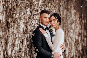 In love bride and groom facing each other, vine wall in background, sunset light, romantic, Lake Taupo. Tuxedo, designer dress.