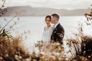 Happy bride and groom leaning against each other in reeves, sunset light, romantic, Lake Taupo.
