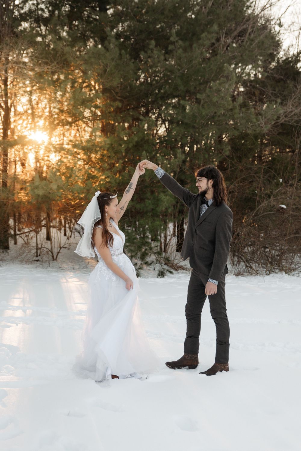 A romantic winter wedding photo of a couple dancing in the snowy forest at sunset.