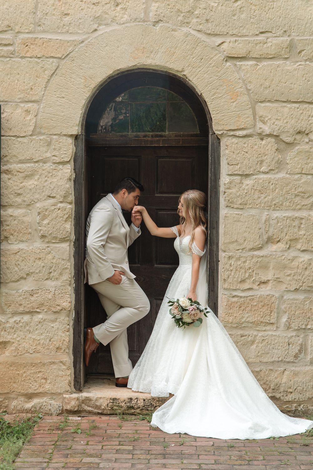 Bride and groom share a romantic moment in an arched stone doorway, bride holding a bouquet in a white gown.