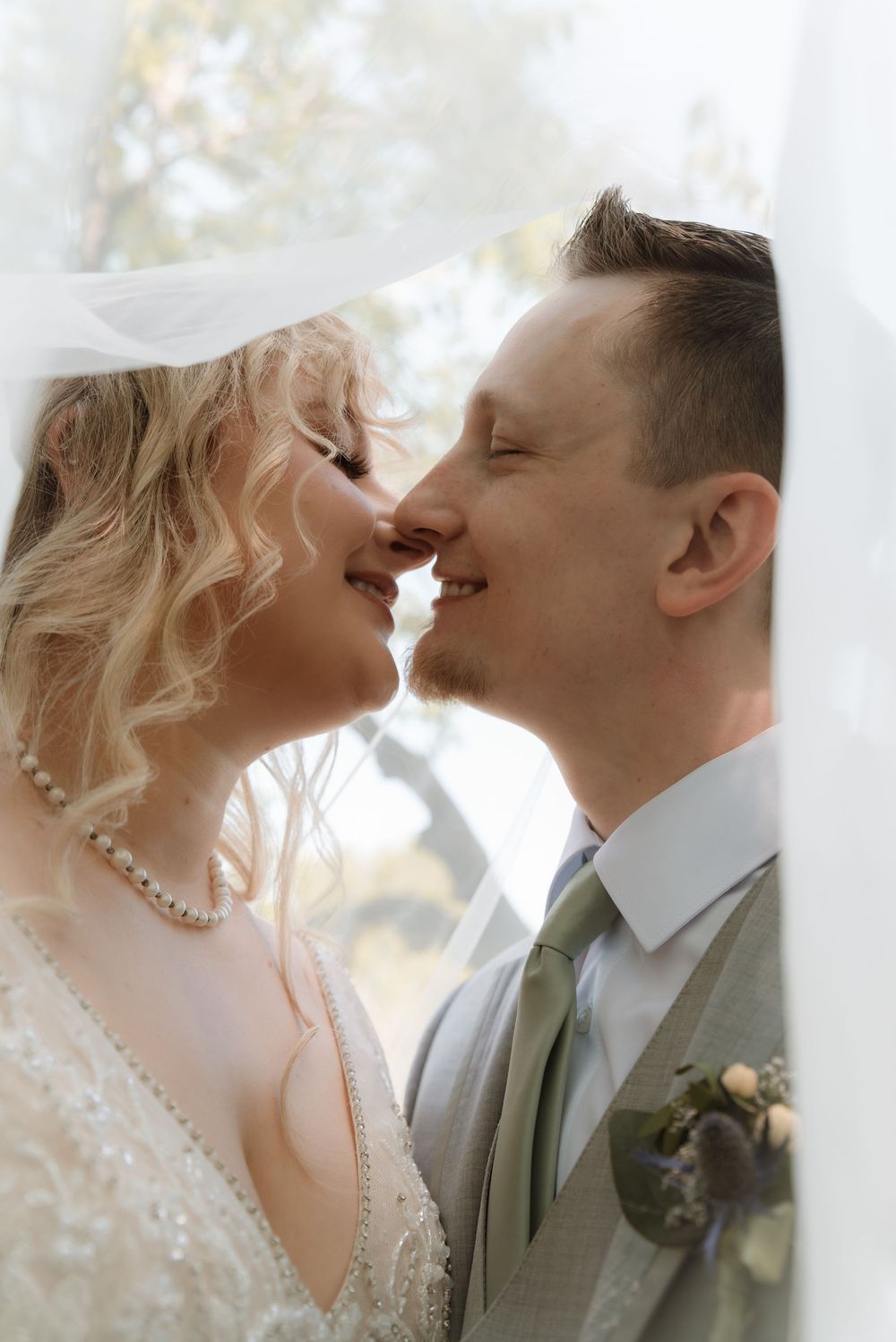 A bride and groom share a romantic almost-kiss under a flowing veil on their wedding day.