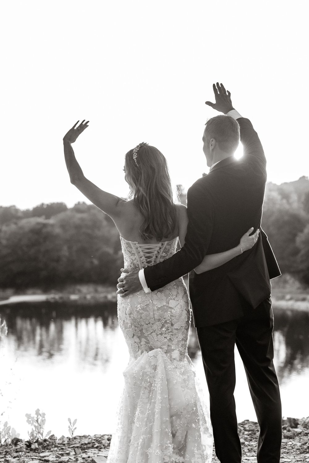 Silhouetted couple raises hands in celebration against sunset lake backdrop.