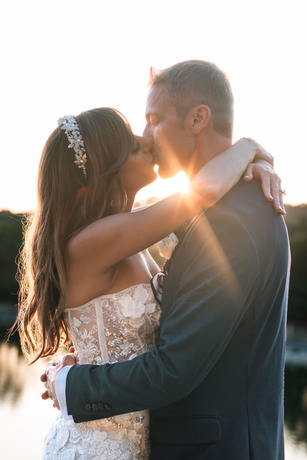 A romantic sunset silhouette of a couple embracing on their wedding day with sunlight streaming between them.