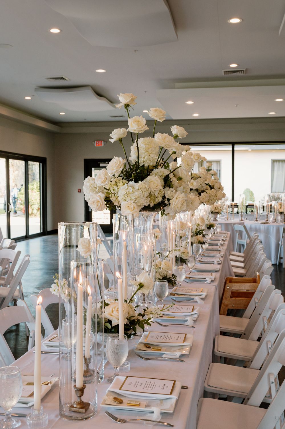 Luxurious wedding reception table settings with tall white floral centerpieces and crystal glassware.