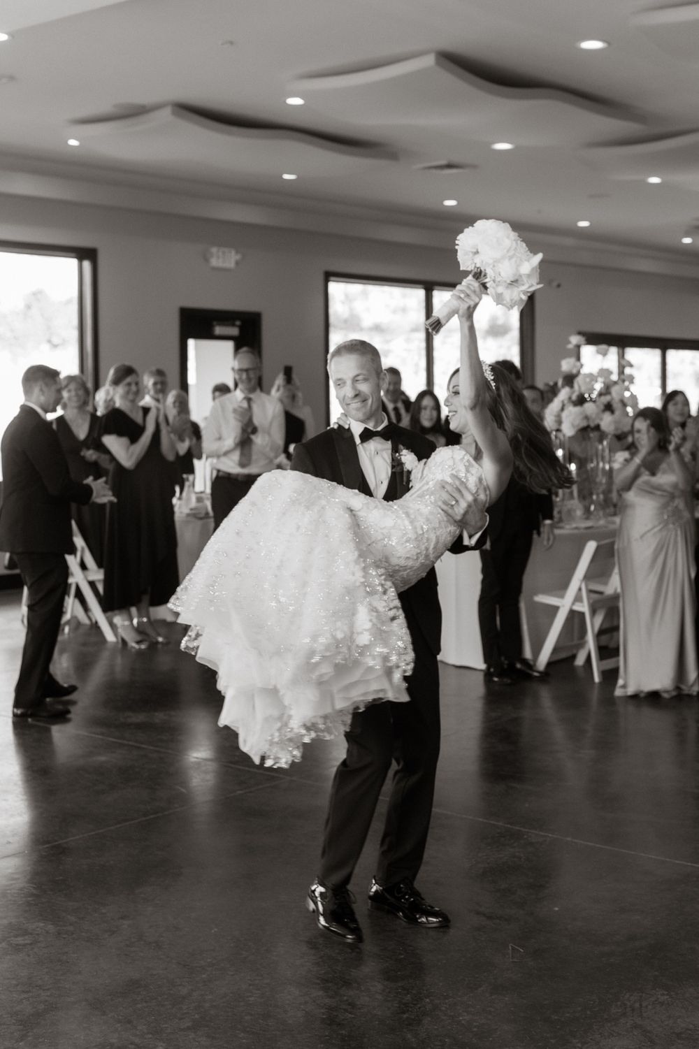 Wedding guests dancing and celebrating on dark reception floor with flowing white dresses.