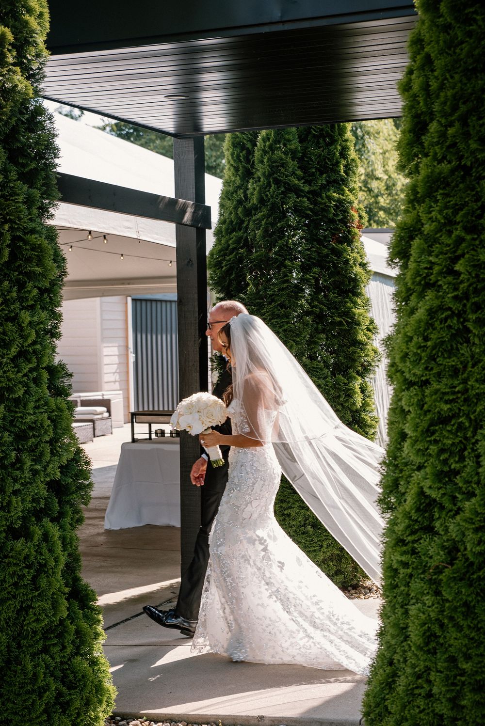 Elegant bride and her father share a dramatic moment outdoors between tall cypress trees.