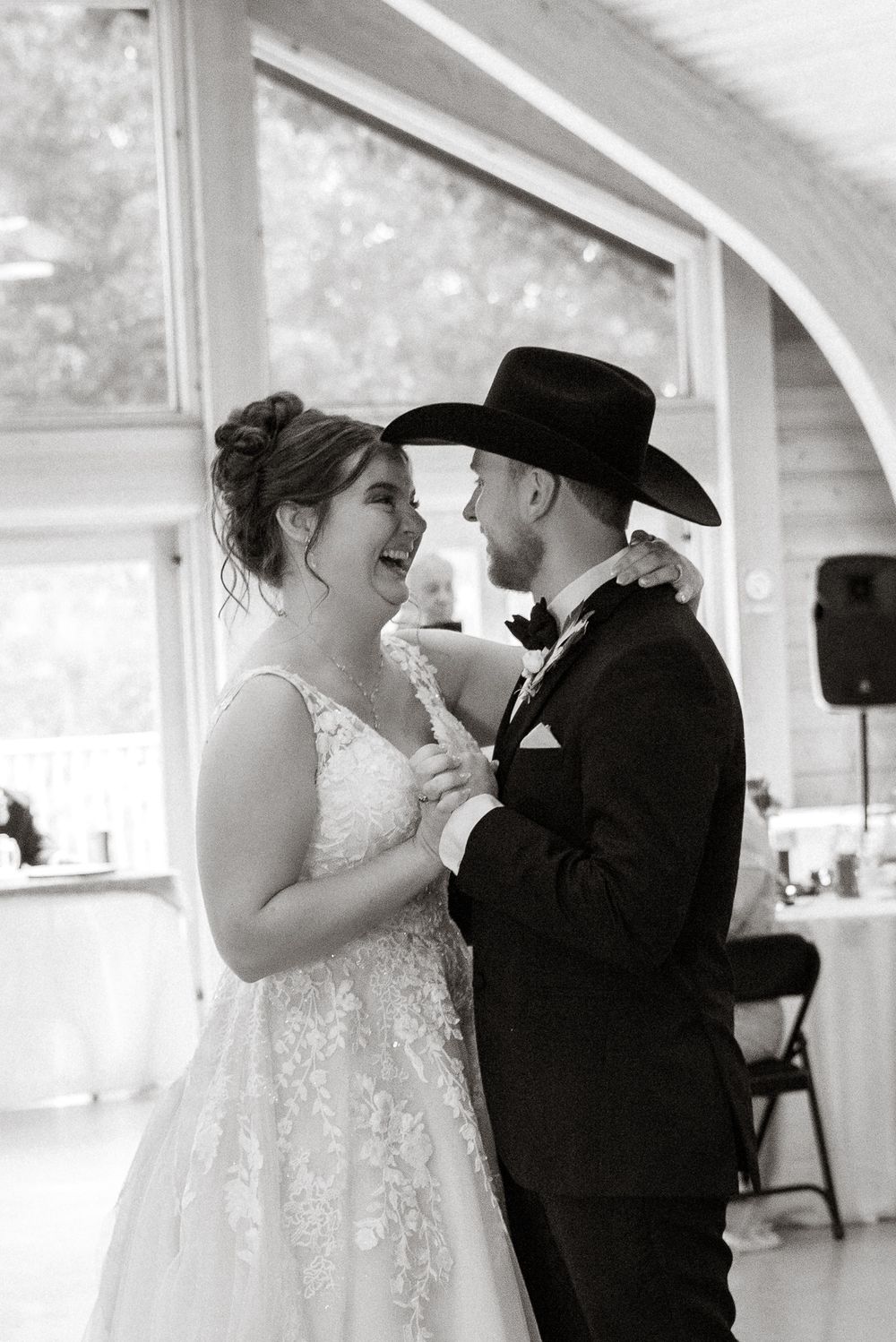 Black and white photo of a bride and groom sharing their first dance at a rustic wedding reception.