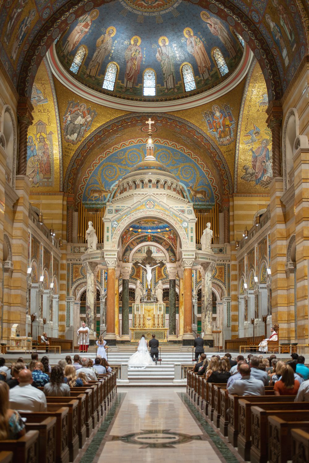 Wedding ceremony inside Cathedral Basilica of Saint Louis with ornate gold mosaics, grand dome, and guests seated in wooden pews.