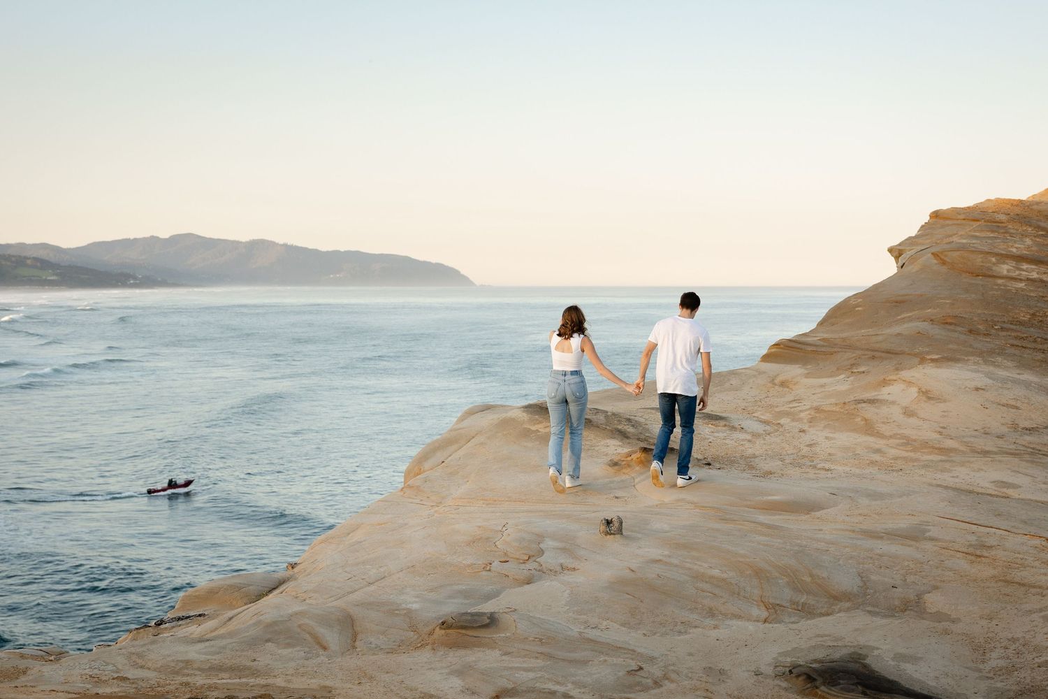 Engaged couple standing on coastal rocks overlooking the pacific ocean at sunrise in Pacific City, Oregon for an engagement shoot.