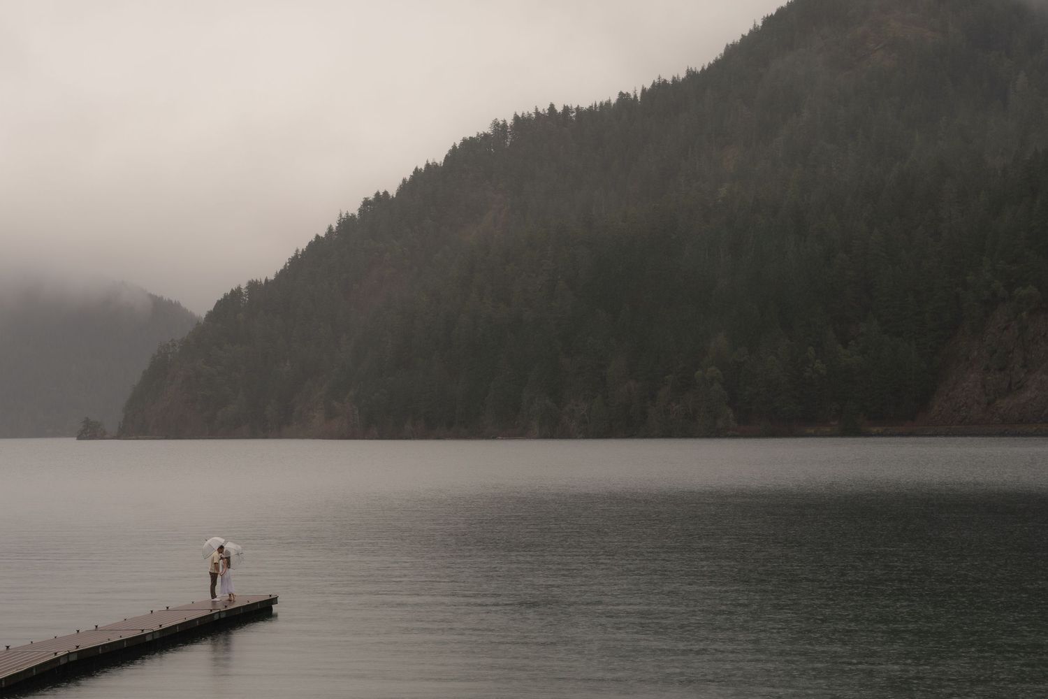 Misty mountain lake view with wooden pier and ducks swimming nearby.