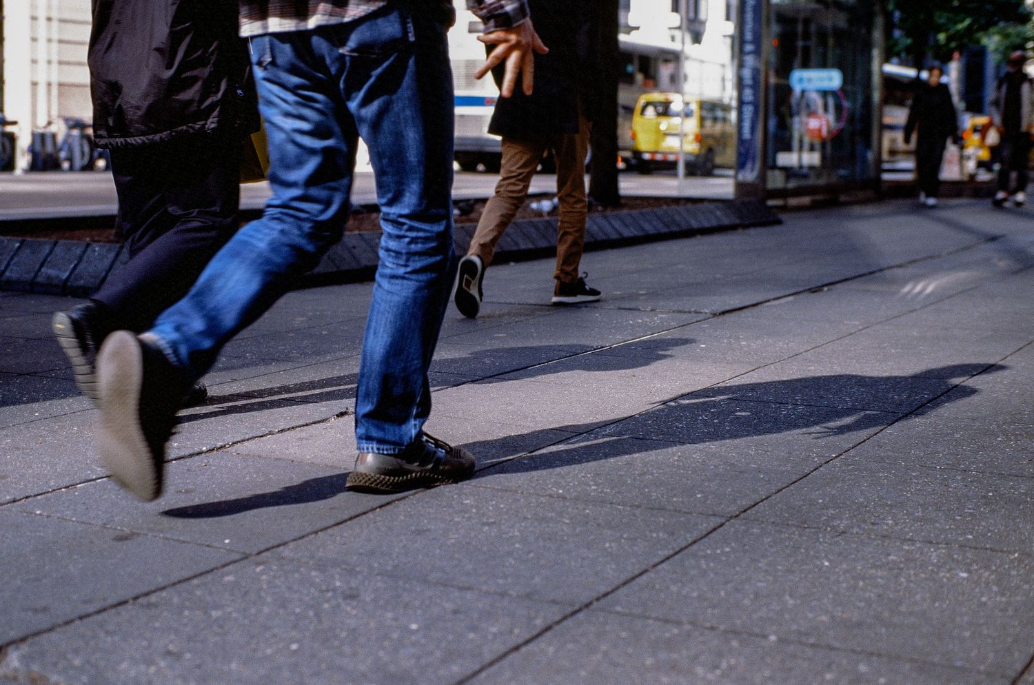 Close-up of pedestrians' feet walking on a city sidewalk in denim and casual shoes.
