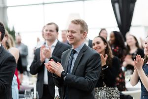 A crowd of formally dressed guests applaud and celebrate at an elegant indoor event.