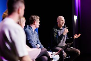 Panel discussion taking place on stage with speakers seated under purple lighting.