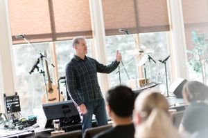 Speaker presenting to audience in classroom setting with window lighting.