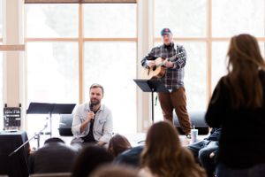 Musicians performing for intimate audience in sunlit room with acoustic guitar.