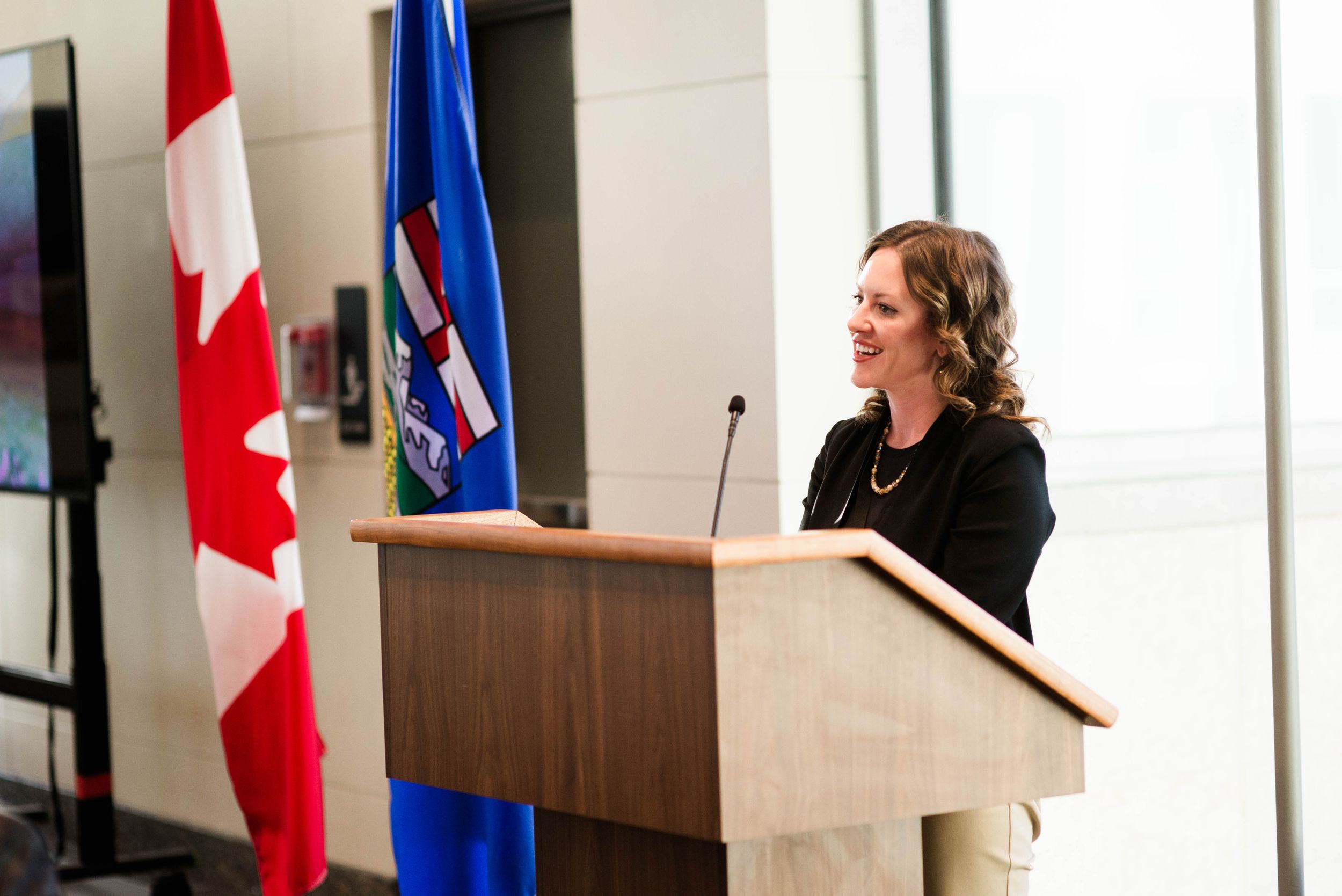 Speaker at podium in front of Canadian flag during formal presentation.