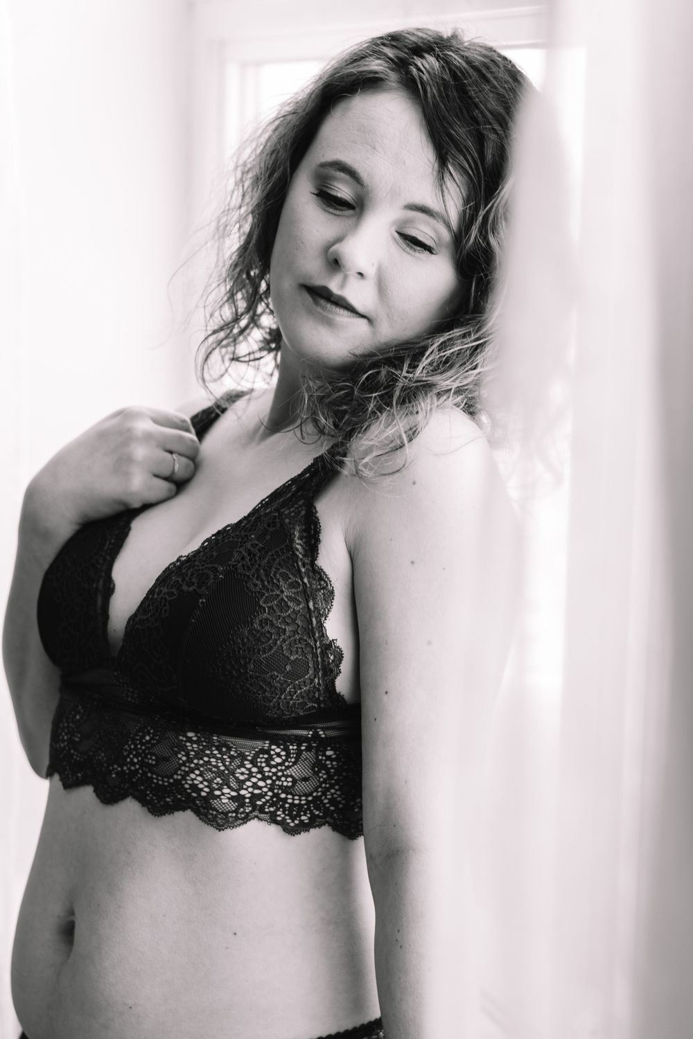 Artistic black and white boudoir portrait showcasing lace bralette against white background.