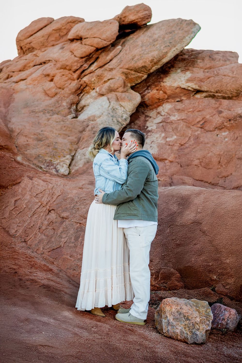 A couple shares a tender moment against dramatic red rock formations in nature.
