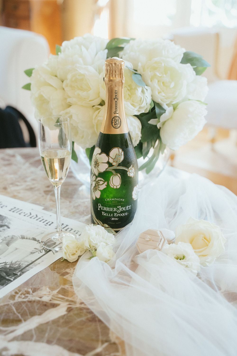 White floral centerpiece with Perrier-Jouet champagne bottle and crystal glasses on elegant table setting.