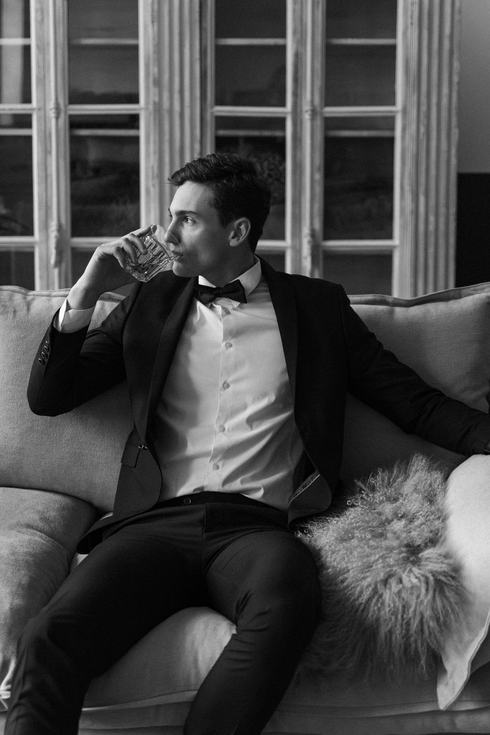 Black and white image showing people in formal attire reclining on a couch in an elegant setting.