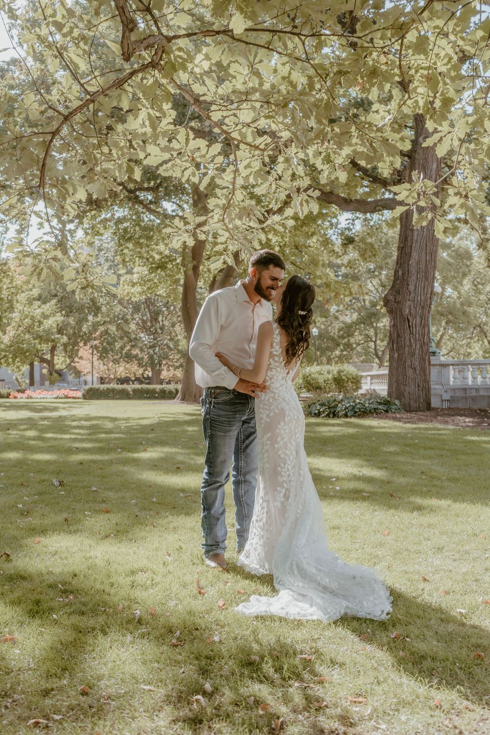 Bride and groom share a tender kiss under a large tree in a green park.
