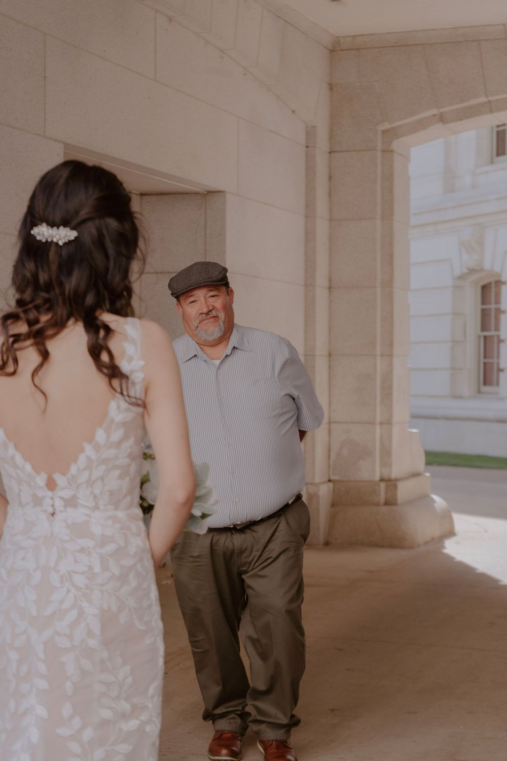 Older gentleman in flat cap shares an emotional first look moment with bride in lace gown.