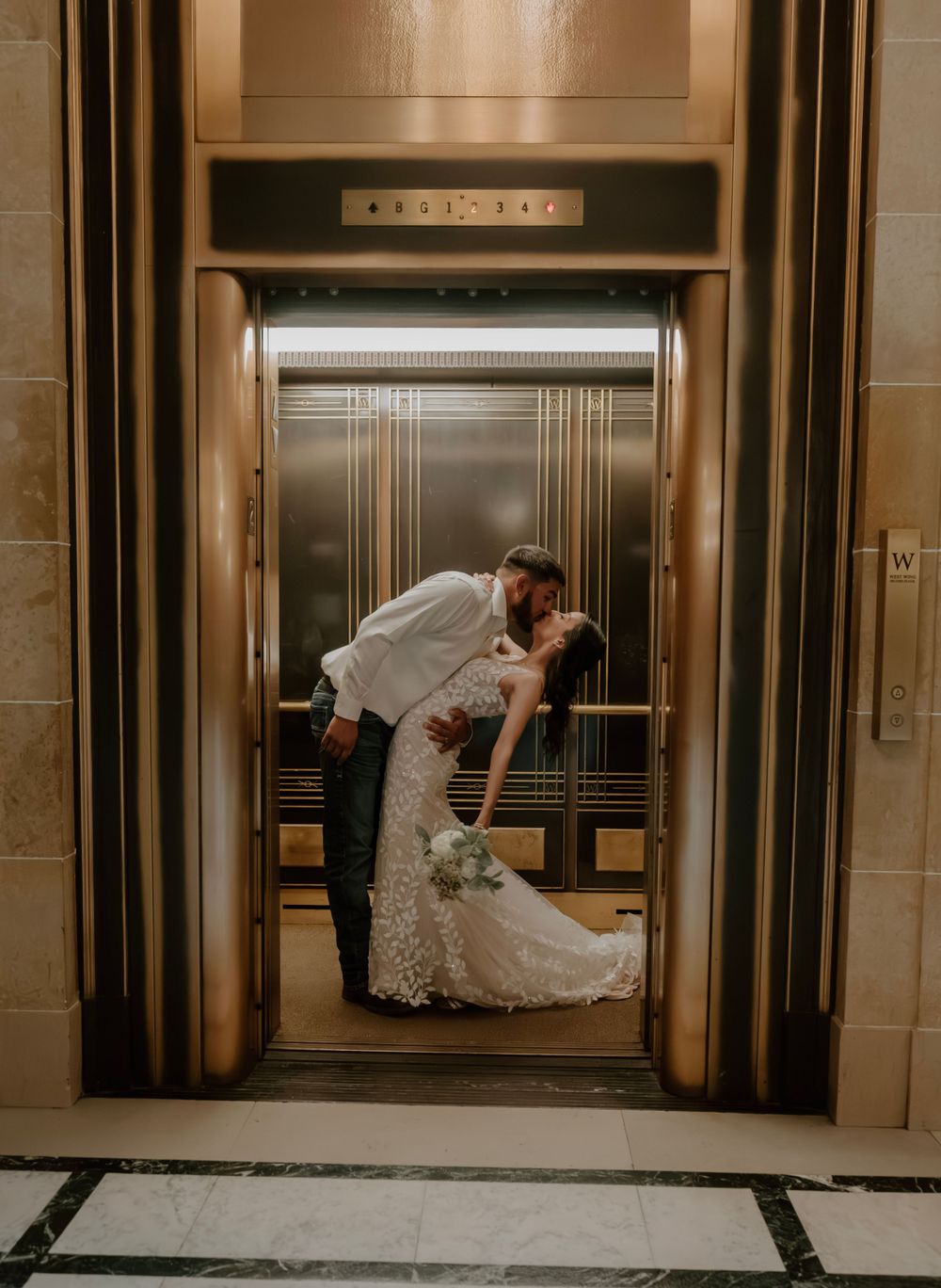 Bride and groom share a passionate dip kiss framed by ornate gold elevator doors.