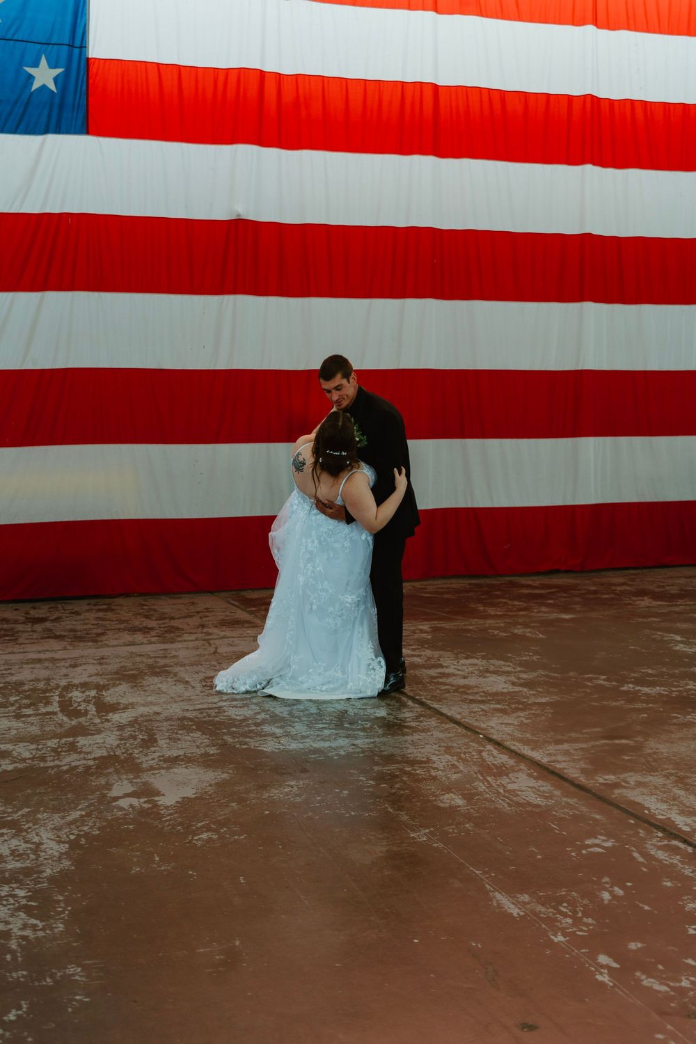 Newlyweds share a romantic dance in front of a large American flag in an aviation hangar.