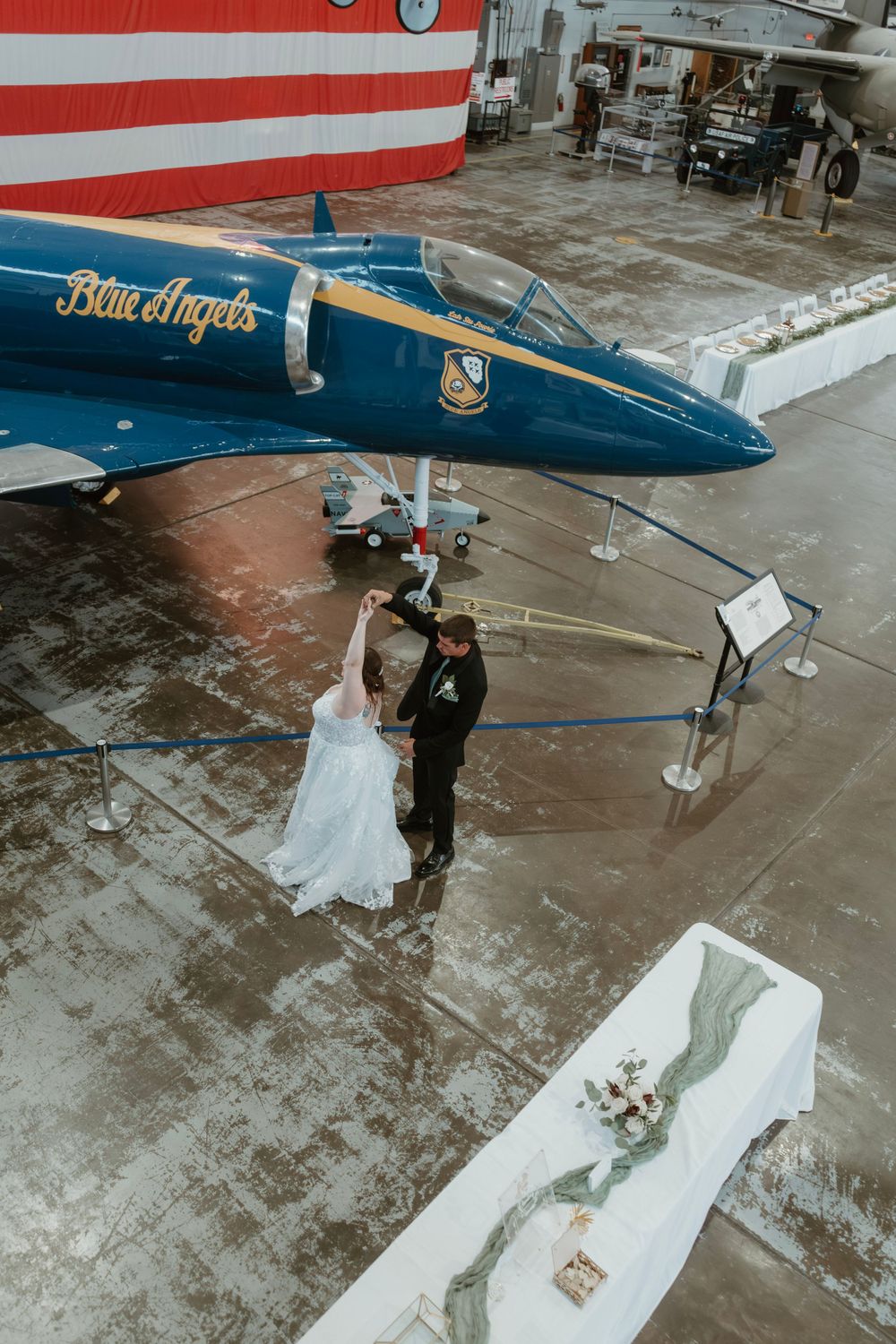 Bride and groom dancing beside a Blue Angels jet inside a stunning aviation museum venue.