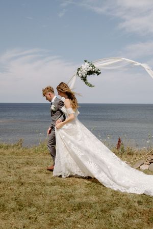 bride and groom walk hand in hand during wedding ceremony on cliff overlooking Northumberland Straight in Nova Scotia, Pugwash
