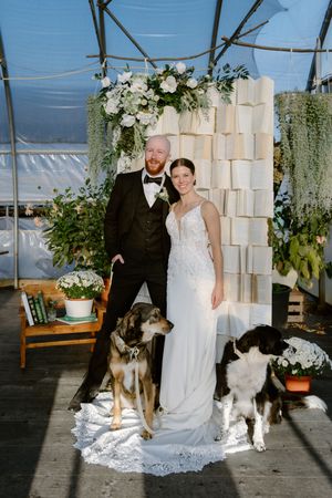 Bride and groom pose infront of DIY wall of books backdrop in fall greenhouse wedding in New Brunswick, Farmer Brown's Greenhouse wedding