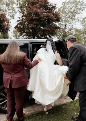 Bride getting into a limo before wedding ceremony while her wife helps her, Rainy October wedding in Cape Breton, Nova Scotia wedding photo