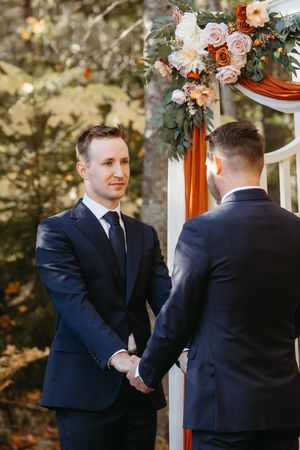 grooms hold hands during wedding ceremony in an intimate outdoor backyard wedding, October wedding photography in New Brunswick, same sex