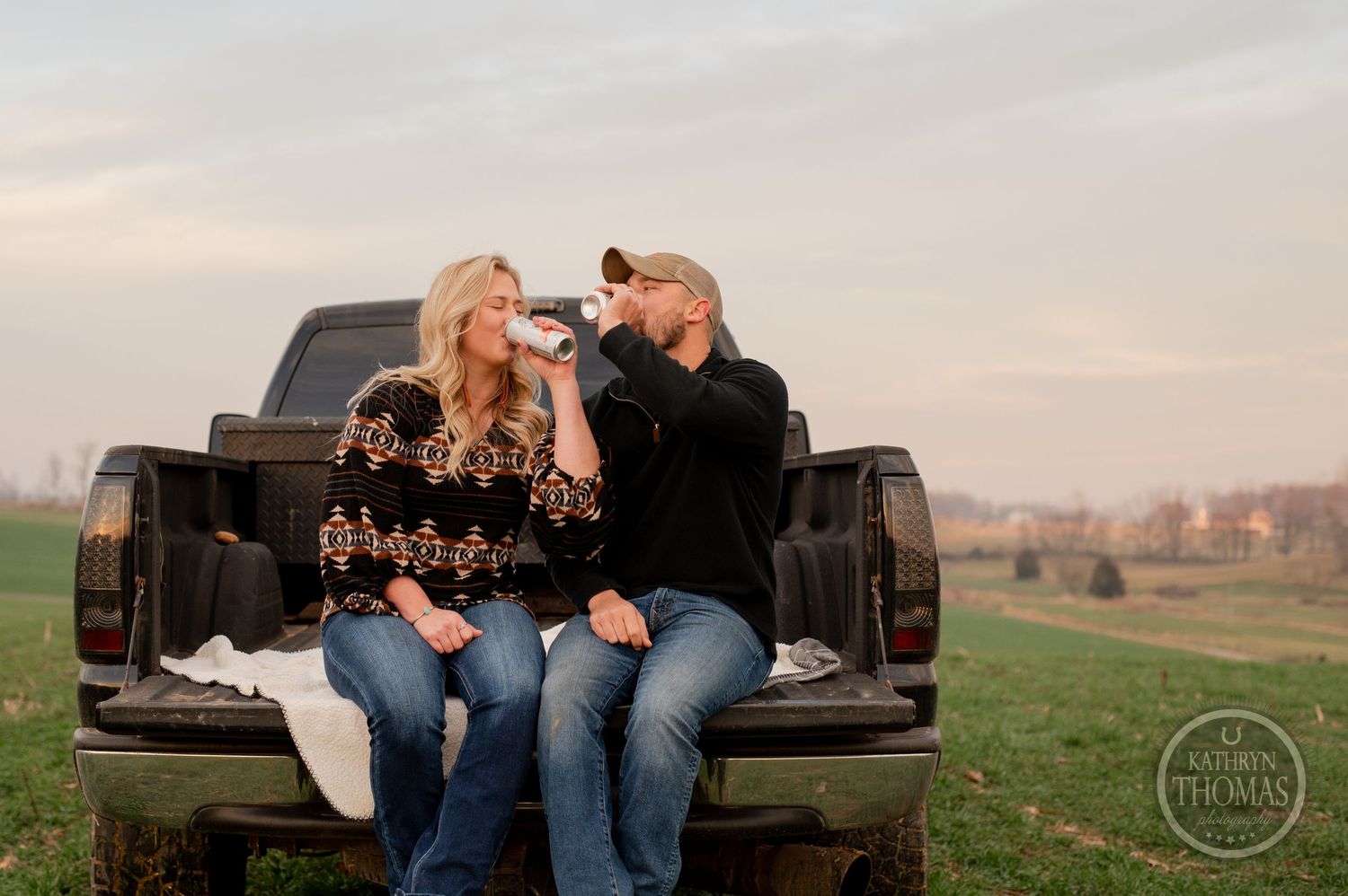 A couple shares drinks and laughter while sitting in the back of their pickup truck.
