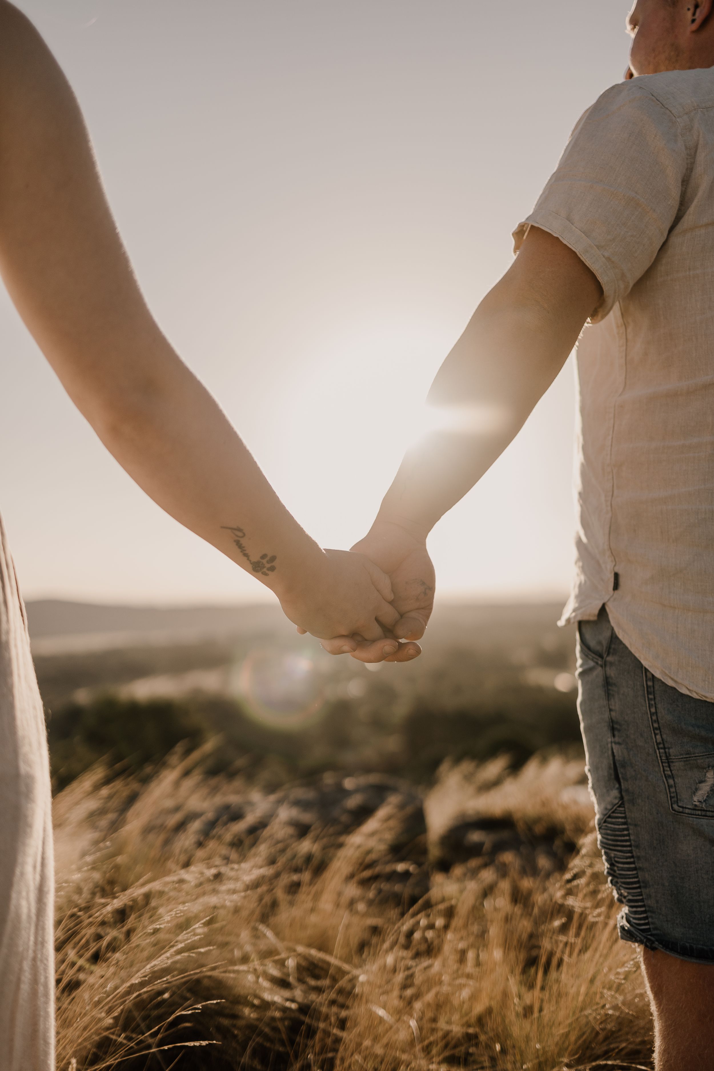Couple holding hands at sunset in a field of golden wheat.