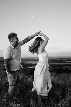 Couple dancing together in a field against a scenic landscape.