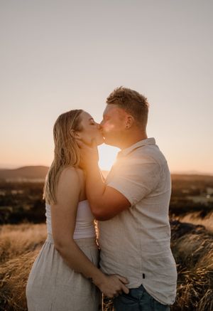 Intimate couple sharing a kiss during golden hour in a rural field.
