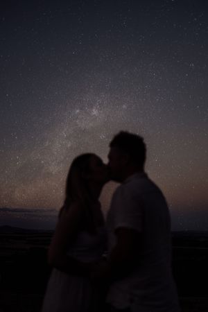 Silhouetted couple kissing under a starry night sky.