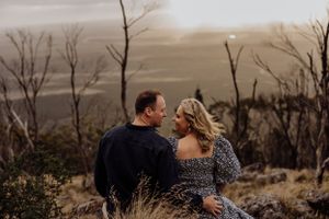 Couple sitting together on a hillside overlooking a misty landscape.