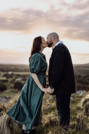 A romantic couple sharing a tender moment at sunset on a hilltop overlooking a scenic landscape.
