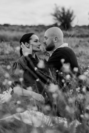 A black and white portrait of a couple sharing an intimate moment among wildflowers in a field.