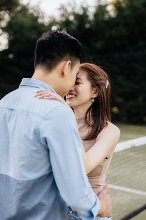 A joyful couple embracing and laughing together on a tennis court on a sunny day.