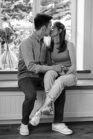 A couple sharing an intimate moment while sitting on a window ledge in black and white.