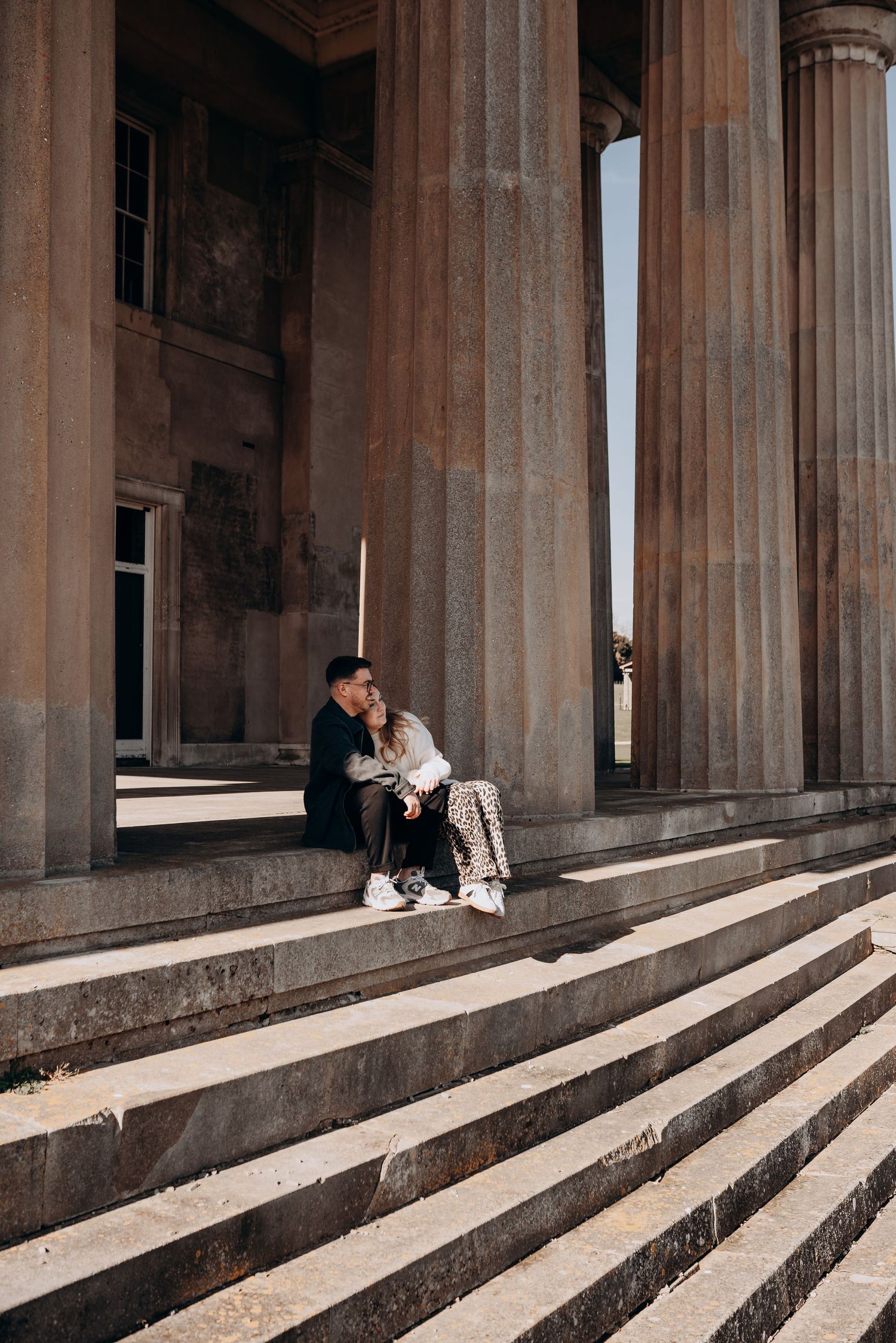Couple sitting on grand stone steps of classical building with columns.