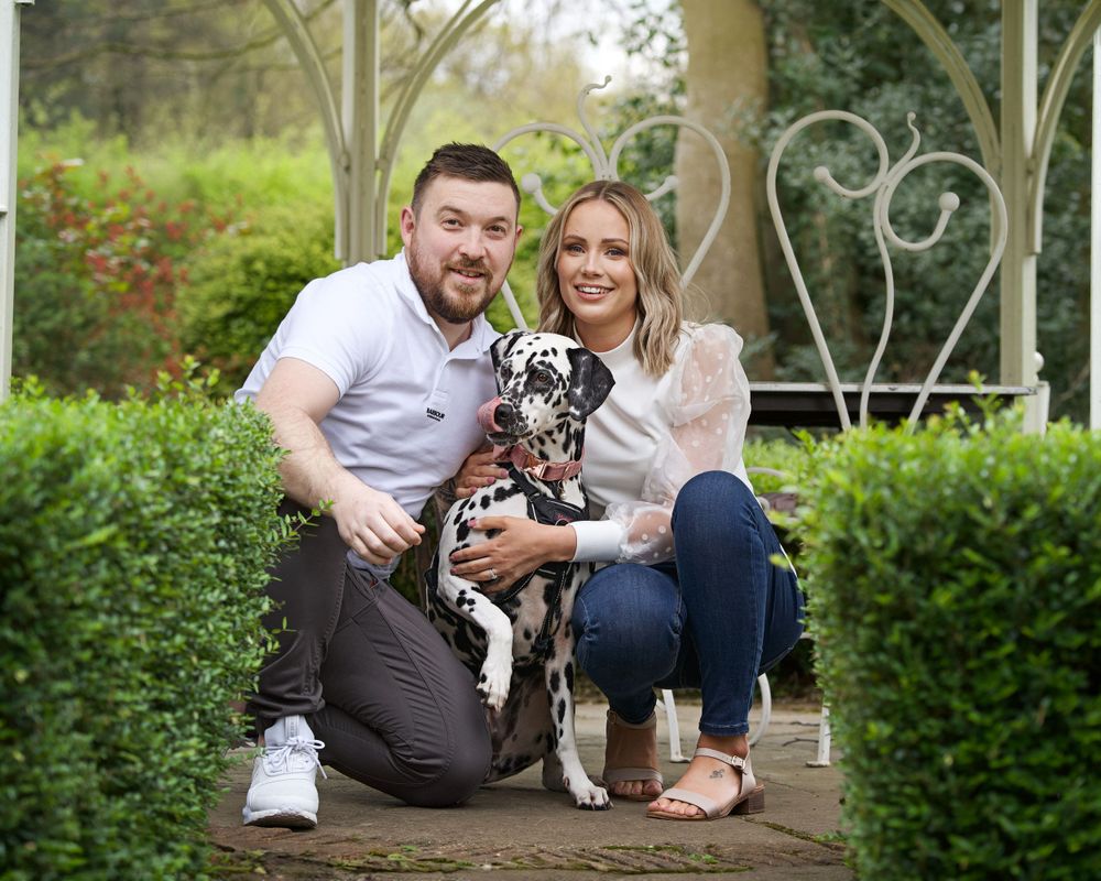 A couple poses with their spotted Dalmatian dog on a garden bench.