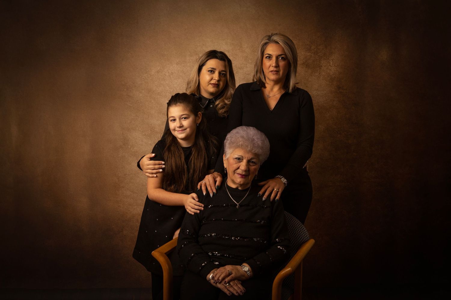 Family portrait with dramatic lighting against dark brown background.