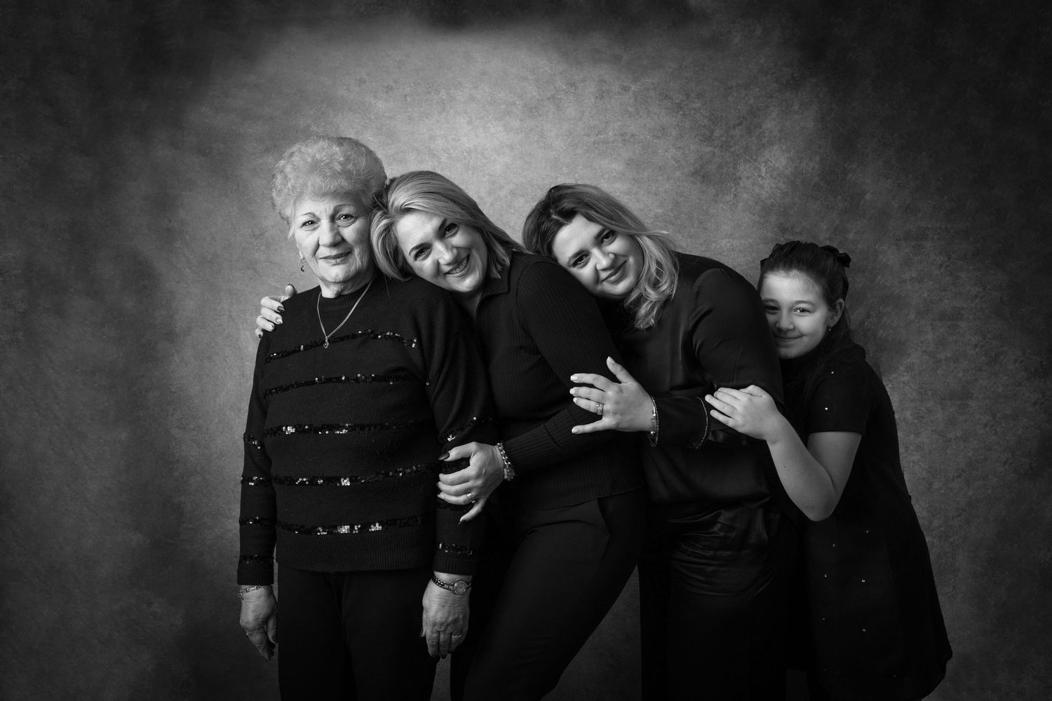 Multi-generational family portrait in black attire against dark background.