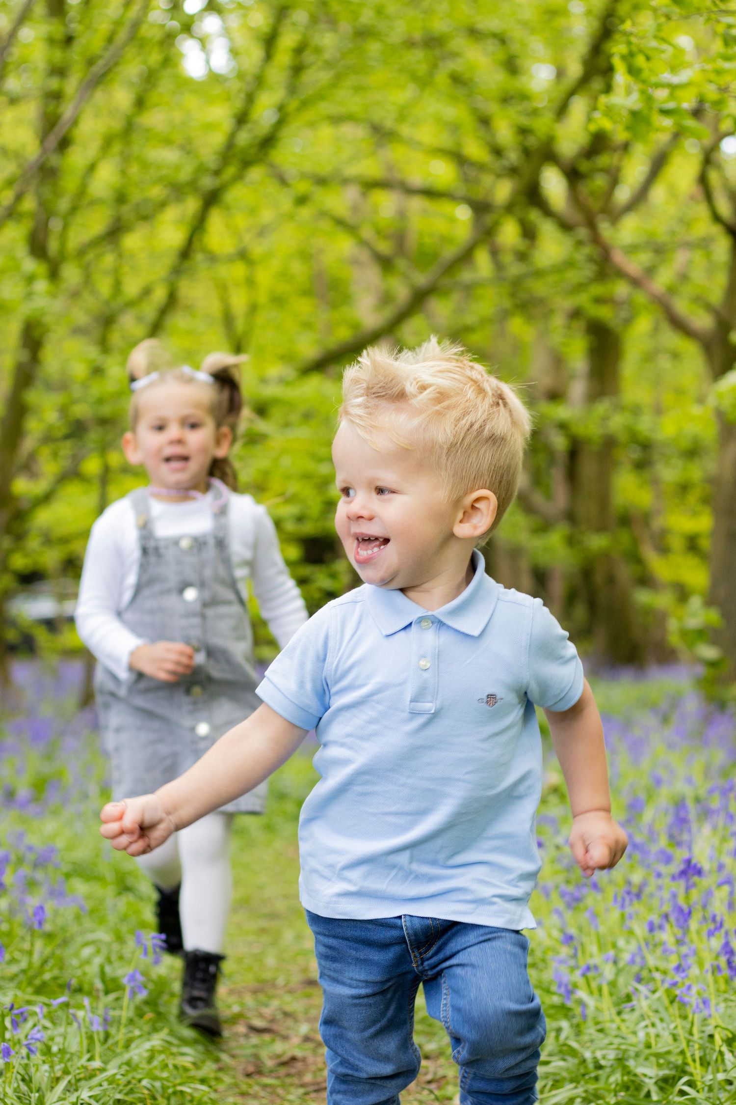 Two children play joyfully among blooming bluebells in a spring woodland setting.